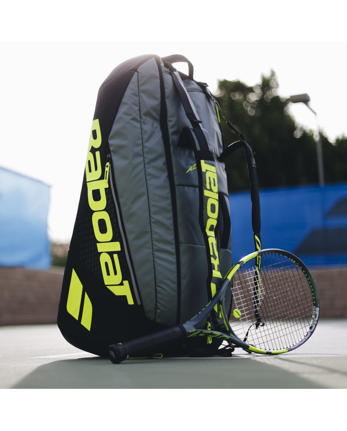 Babolat borsa da tennis nera e grigia con logo giallo fluo, tasche multiple, e racchetta appoggiata accanto.