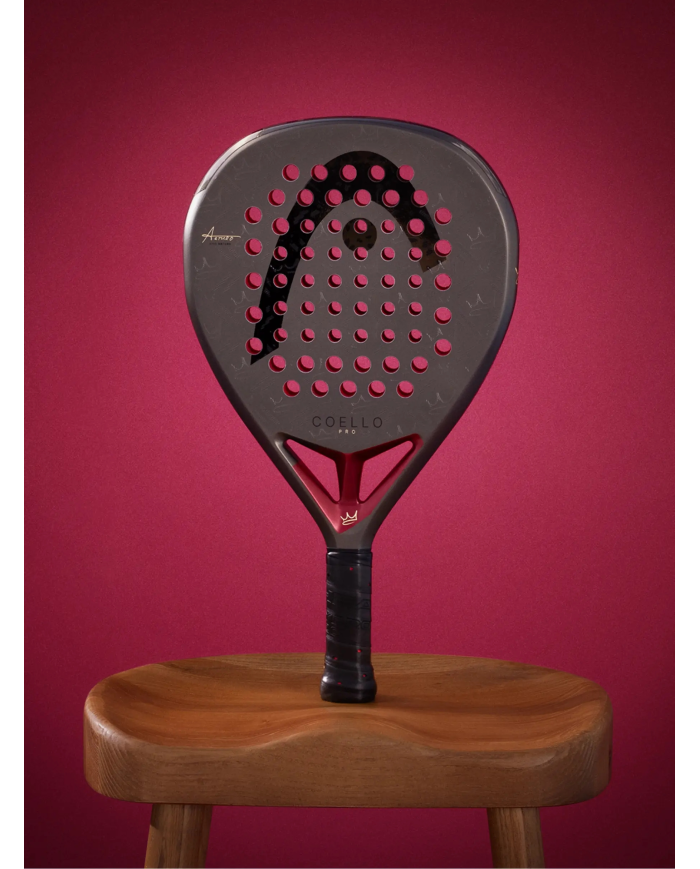 Pala da padel Head Coello Pro 2026, con fori rossi su superficie nera, impugnatura nera, in piedi su sgabello di legno.