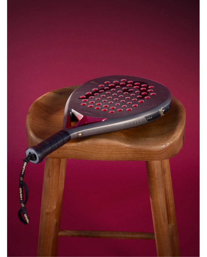 Paddle da padel Head Coello Pro 2026 appoggiata su uno sgabello di legno, in primo piano, sfondo rosa viola.